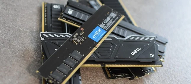 Pentes de memória RAM das marcas Crucial e GeIL empilhados sobre uma superfície cinza, mostrando detalhes dos módulos e chips de memória.