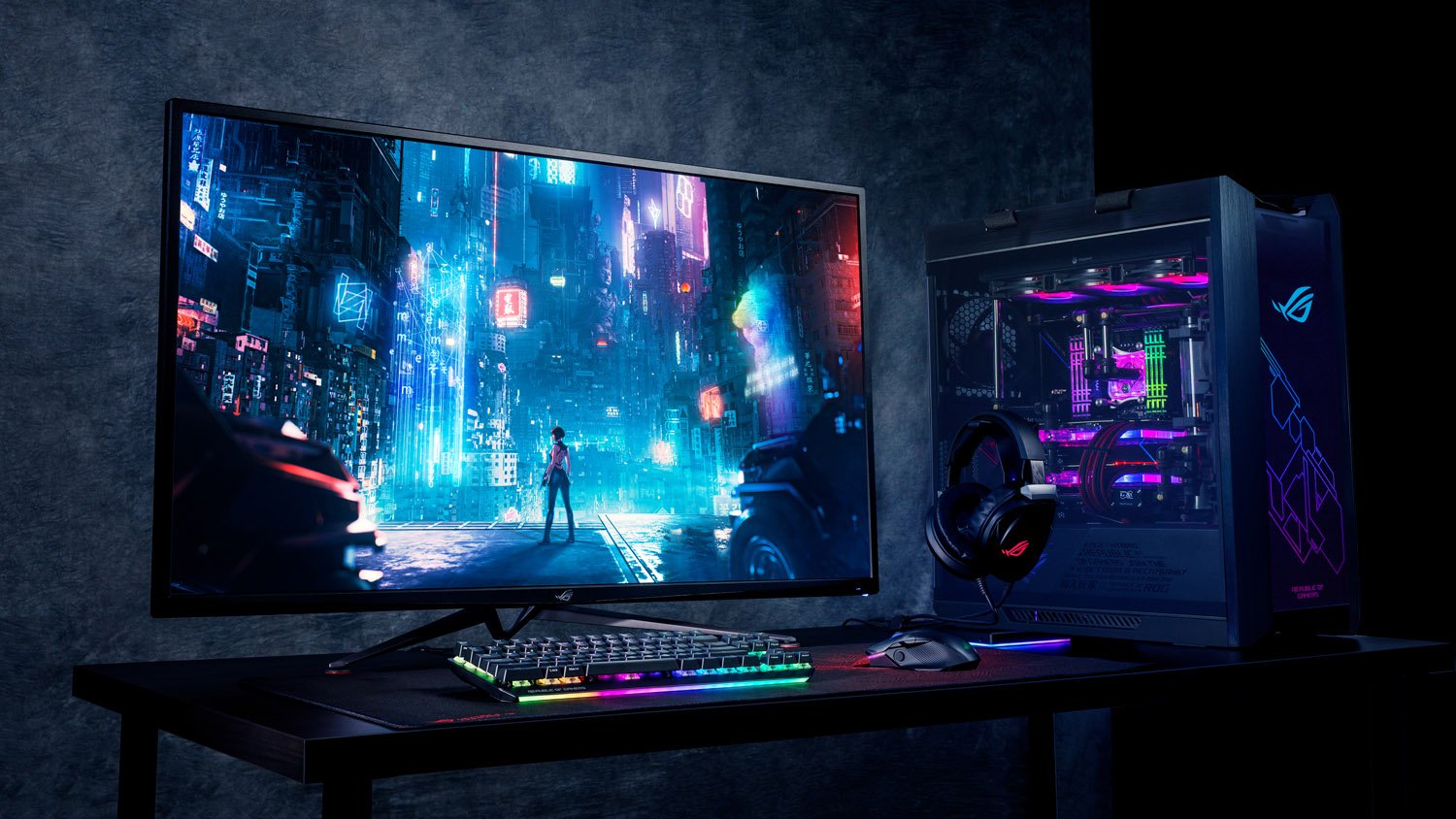Setup gamer completo da ASUS ROG com monitor widescreen, PC desktop com iluminação RGB e periféricos em ambiente escuro.
