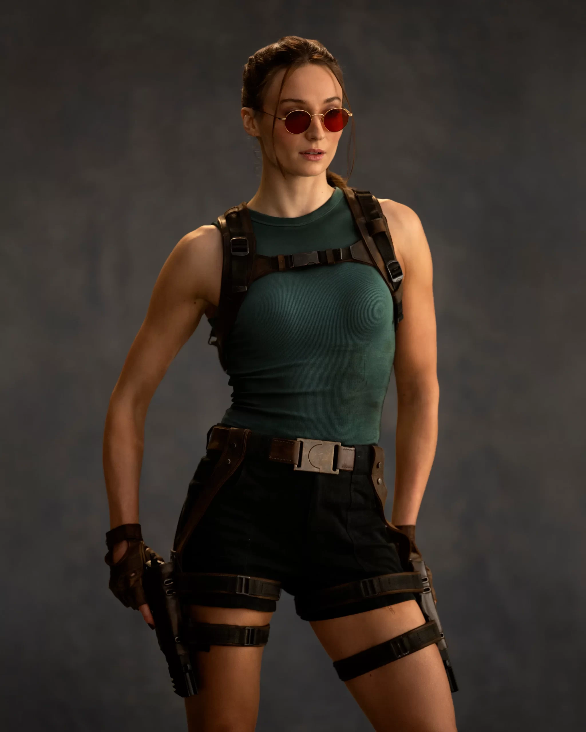 Sophie Turner caracterizada como Lara Croft, com óculos de sol vermelhos e coldres táticos, na primeira foto oficial da série Tomb Raider da Amazon Prime Video